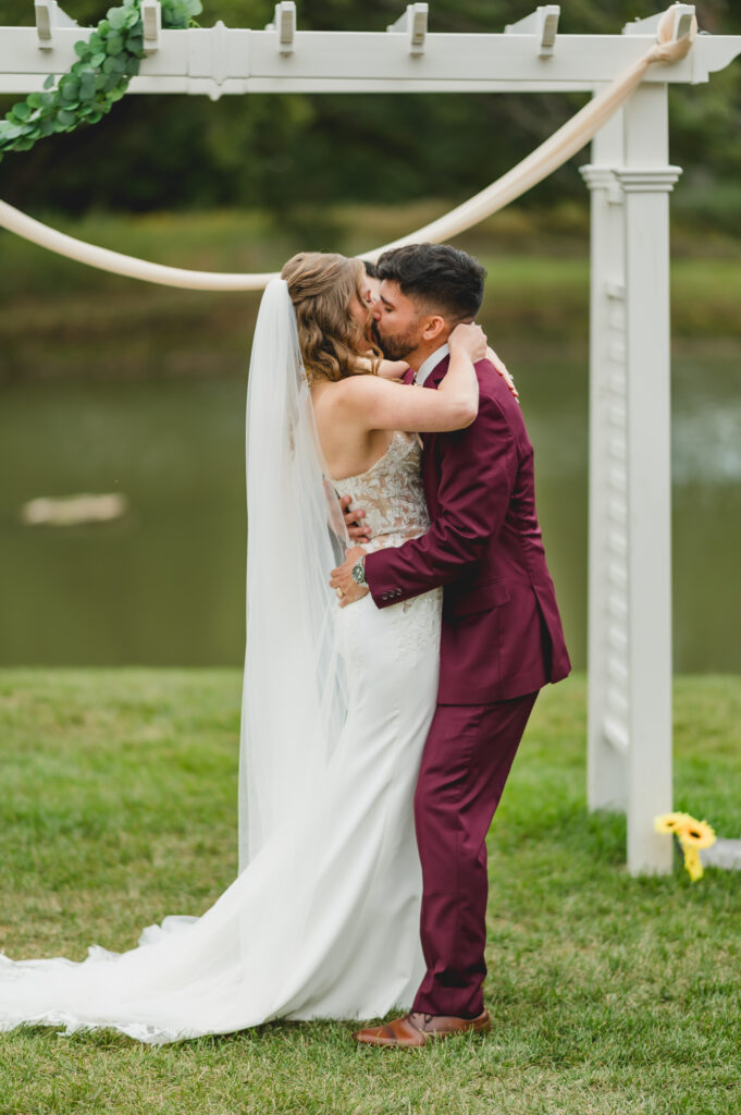 Bride and groom's first kiss at Oakbrook Manor during an outdoor wedding ceremony.