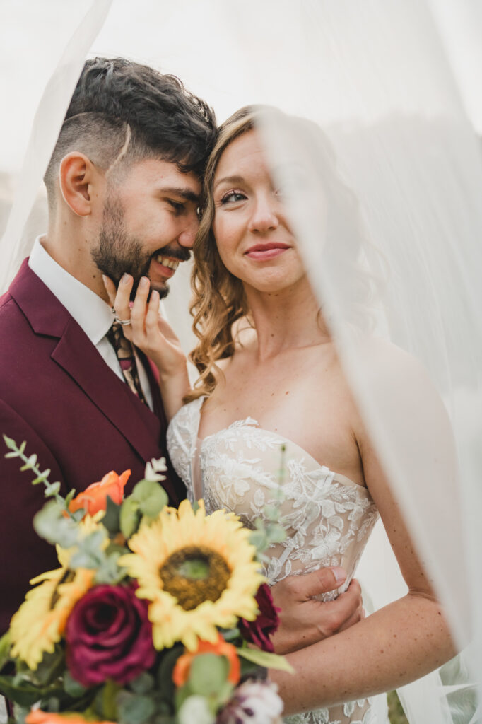 Bride and groom posing for their romantic couple photos under the veil.